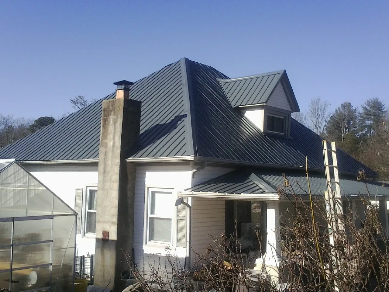 Dark blue standing seam metal roof on a white farmhouse with dormer — Slate & Tile Roof Repair by Roofing Brothers in Opp
