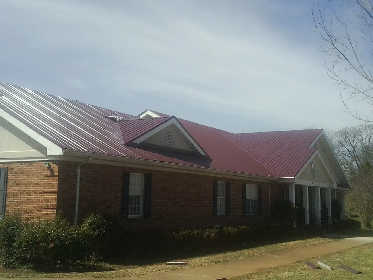 Red metal roof with gabled entries on a long brick building, from a Hail Damage Roof Repair job in Opp