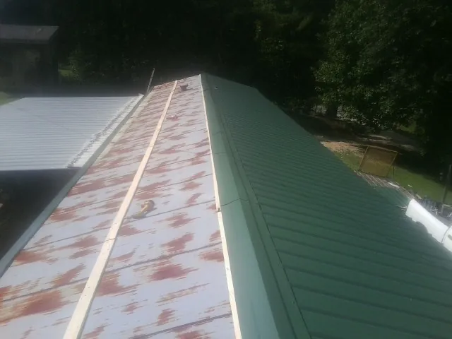 Old rusted panels beside newly installed green metal roofing — Wind Damage Roof Repair by Roofing Brothers in Opp
