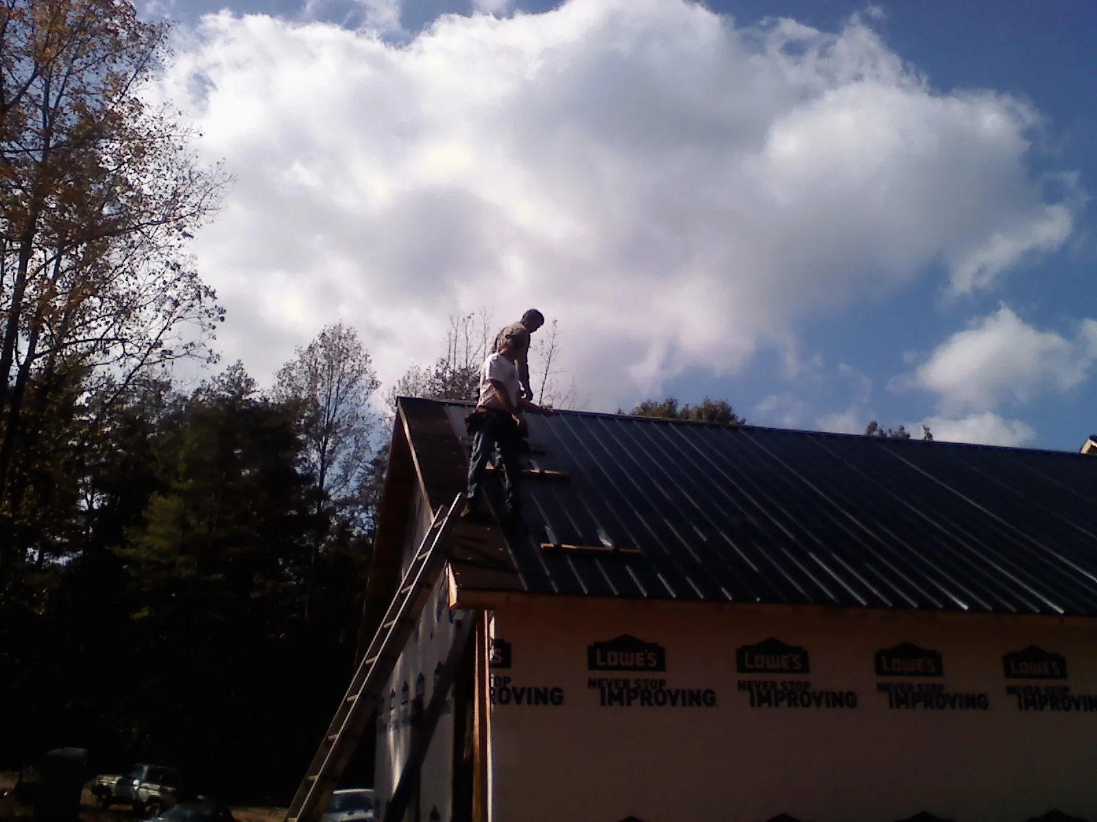 Roofer fastening dark metal panels high against a cloudy sky, from a Roof Inspection job in Opp