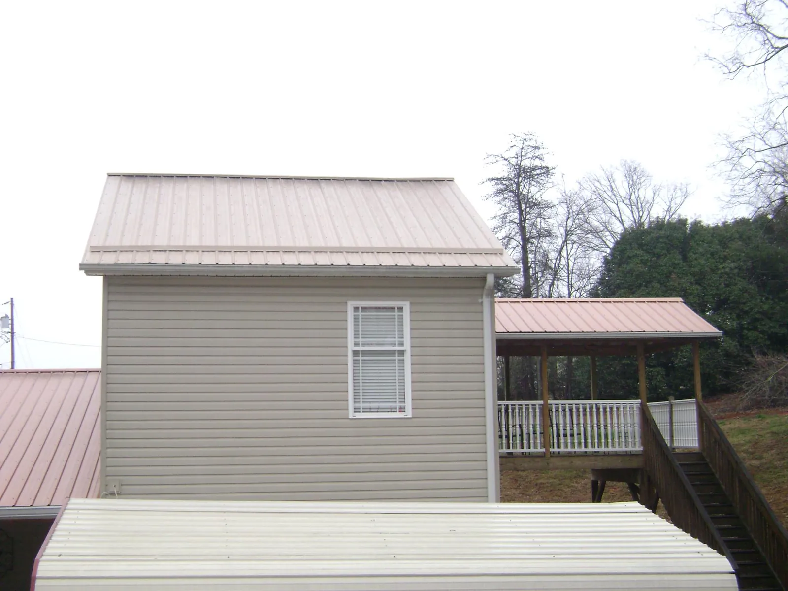 Tan metal roofs on a two story addition and attached porch, from a Roof Replacement job in Opp